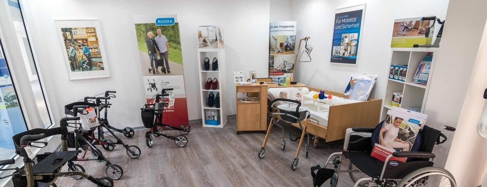 Verkaufsraum mit Gehhilfen, Rollatoren, Rollstuhl und Pflegebett, umgeben von Informationspostern und Regalen mit Produkten